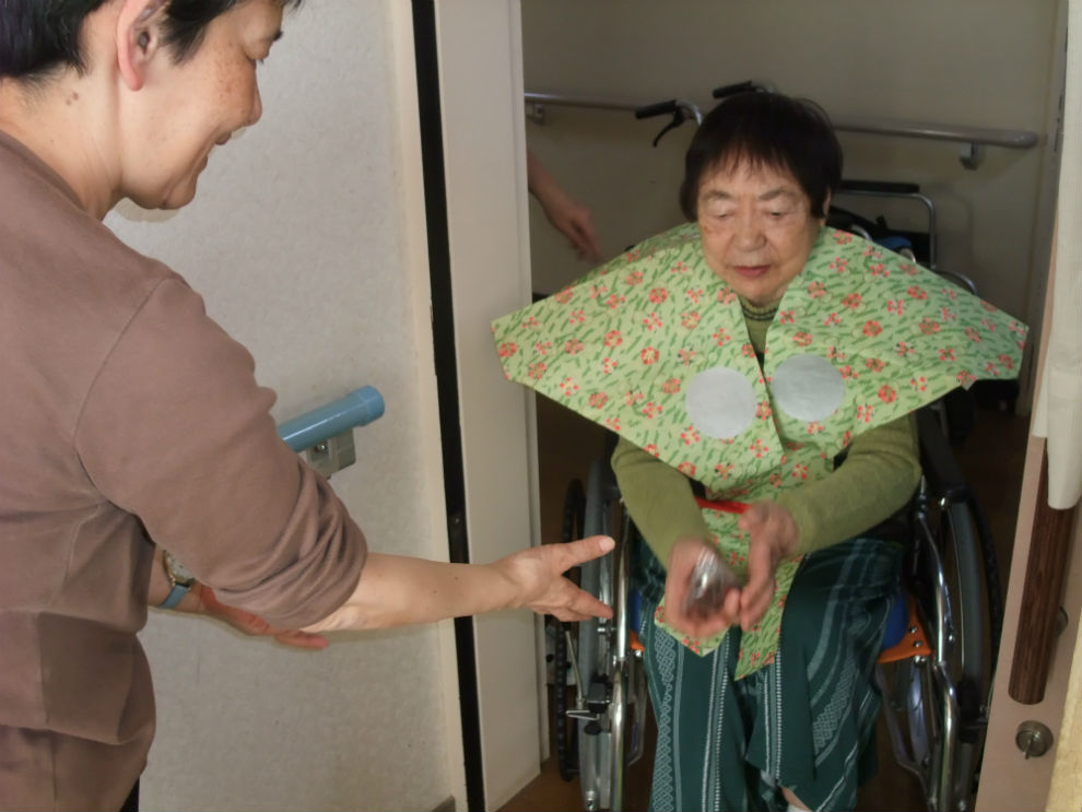 車椅子に乗った年女の方から甘納豆が入った小袋を受け取っている女性の様子