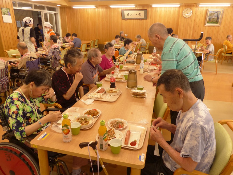 夏祭りで提供したお好み焼きなどを食べている利用者様の様子