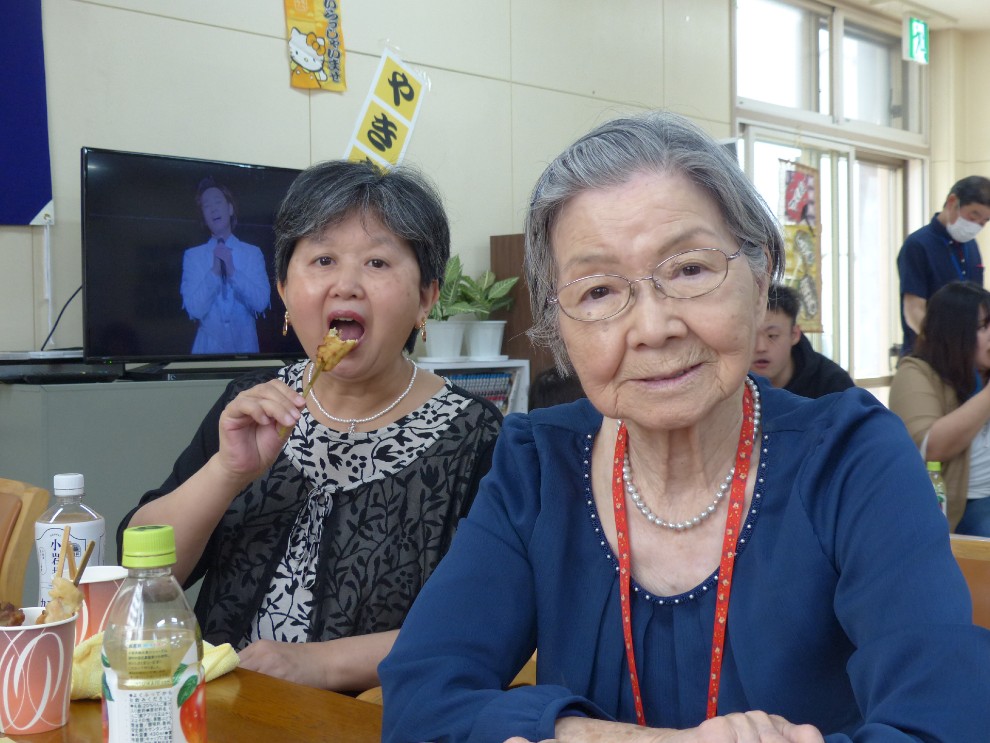 開設記念行事で提供した焼き鳥を頬張る二人の女性利用者様