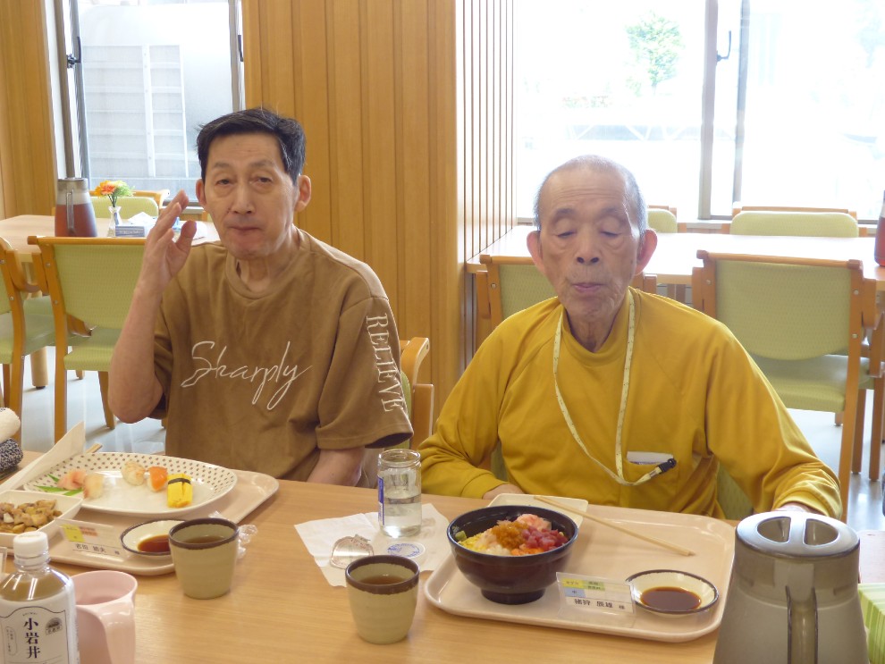 開設記念行事で提供したお寿司を前に記念撮影する二人の男性利用者様