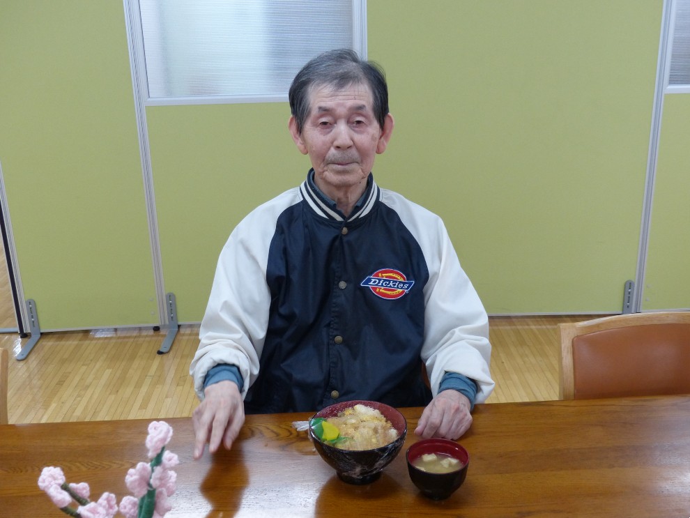 出前レクで料理を前に微笑んでいる男性利用者様