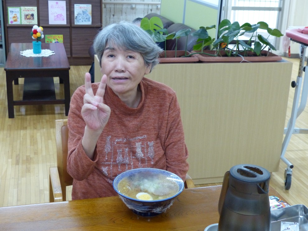 出前レクで料理を前にピースサインをする女性利用者様