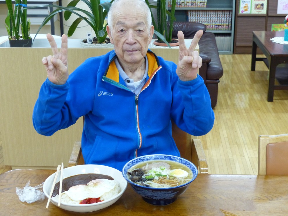 出前レクで料理を前に両手でピースサインをする男性利用者様