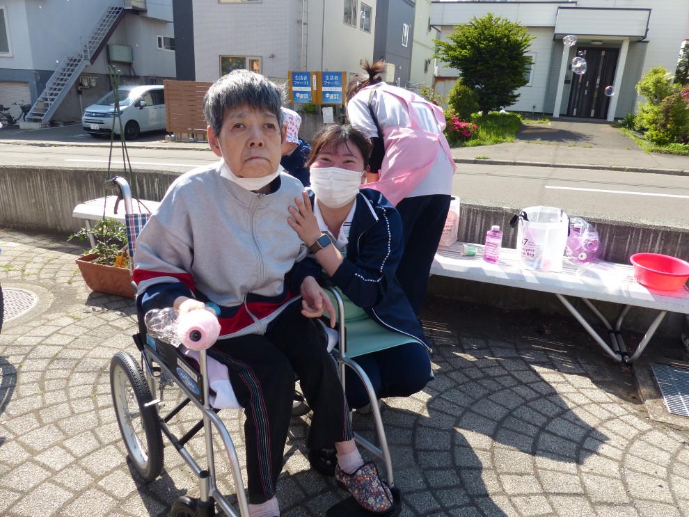 施設の中庭でシャボン玉を楽しむ車椅子の女性利用者様と女性職員で記念撮影