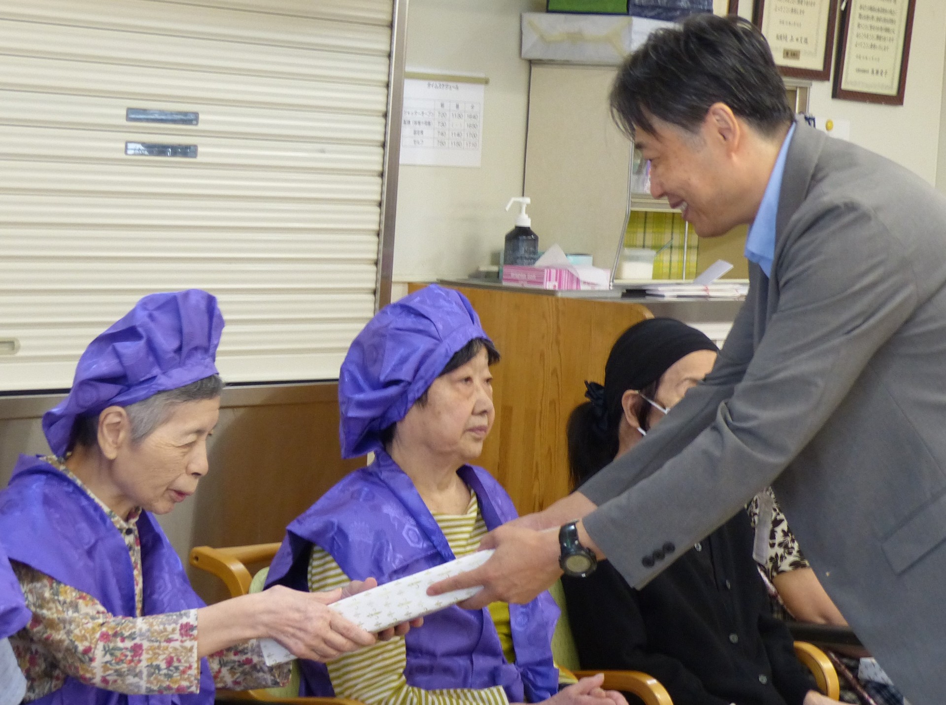 敬老会でお祝いを受けた女性利用者様が記念品を受け取る様子