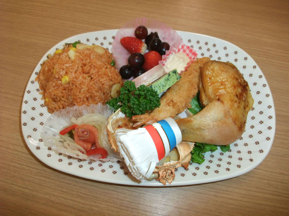 昼食メニューの写真です。野菜と魚介たっぷりのケチャップライス、テリーヌ、カニ甲羅グラタン、エビフライ、チキンレッグちょっぴり和風味、フルーツなどです。