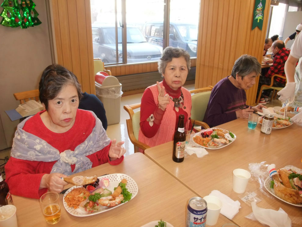 二人の女性がクリスマス会の料理を前にピースサイン。