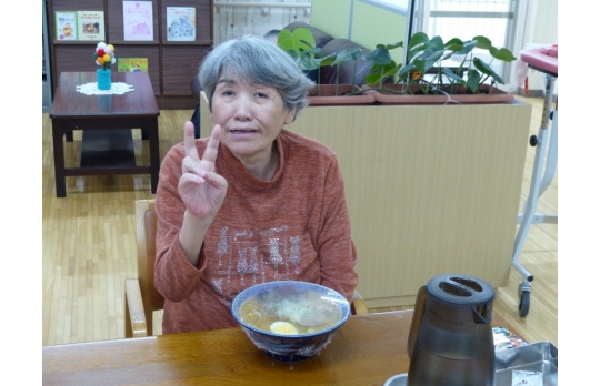 出前レクで料理を前にピースサインをする女性利用者様