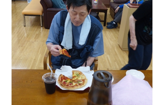 出前レクで頼んだピザを食べようとする男性利用者様